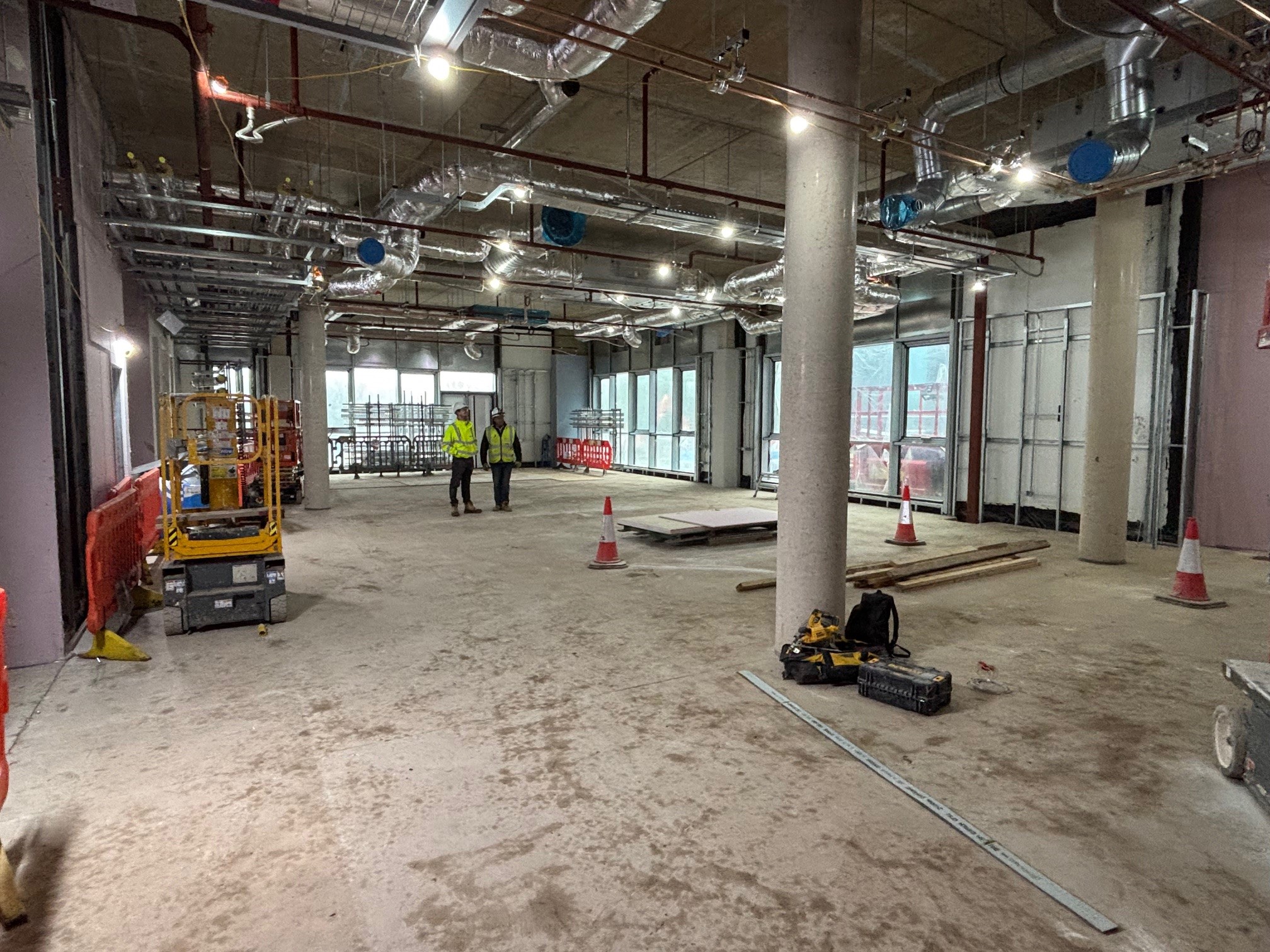 Two men in hi-vis jackets in the bare canteen under construction