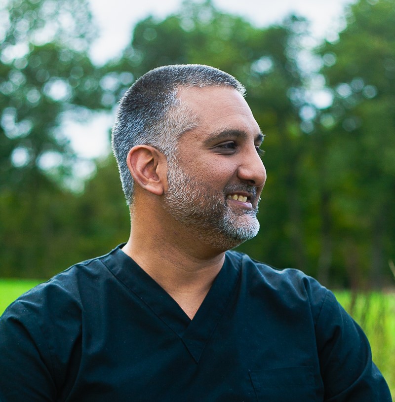 A man in black scrubs smiles to someone off screen
