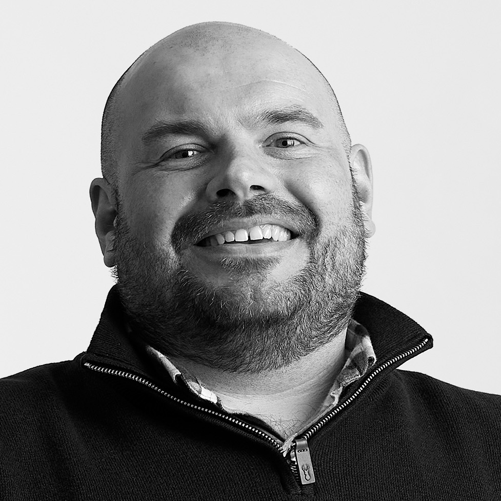 A man with a beard smiles at the camera. Photo is in black and white
