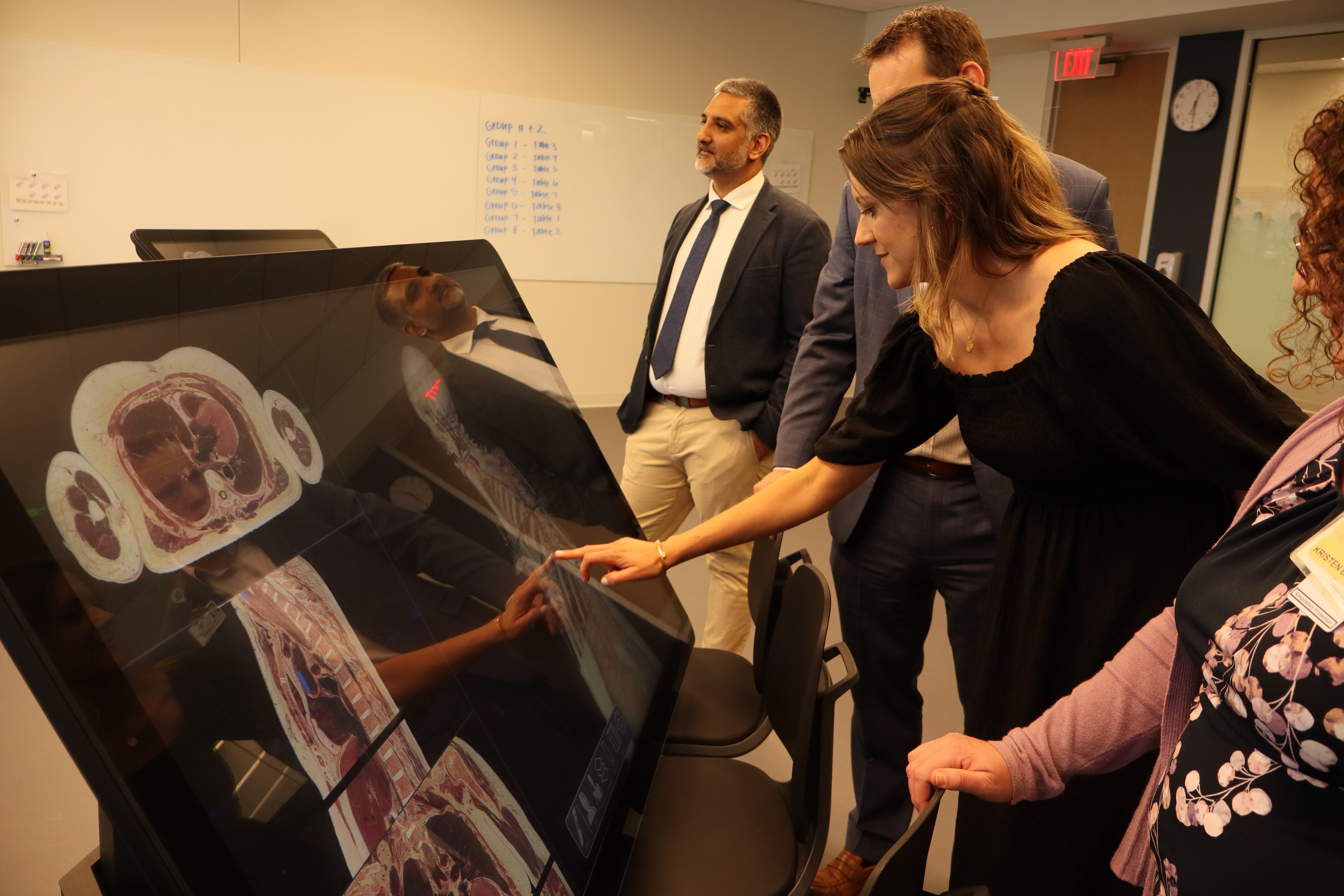 A woman presses with her finger on a screen as other people watch.