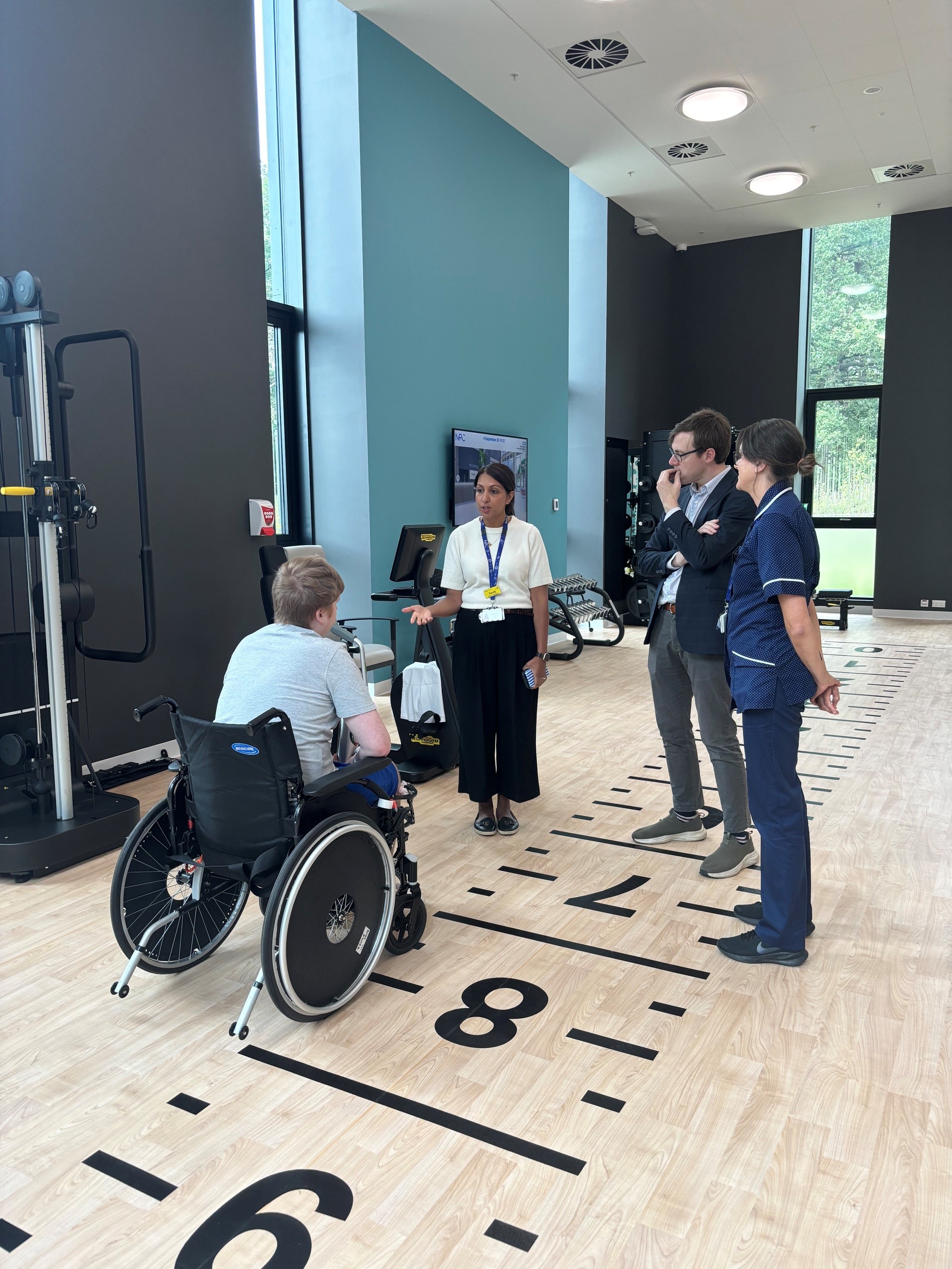 A young man in a wheelchair speaking to three people in a gym