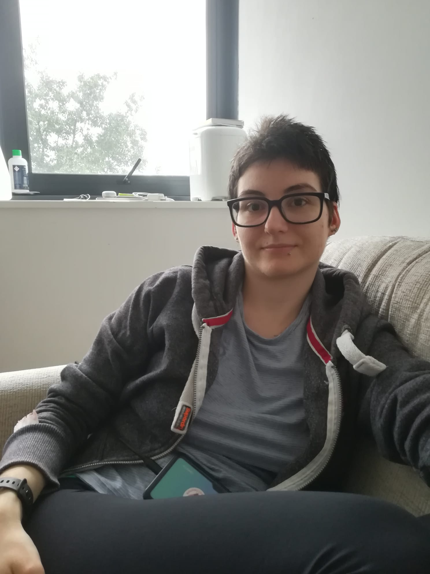 Nora sat on a sofa at home, she is wearing a hoodie and t-shirt