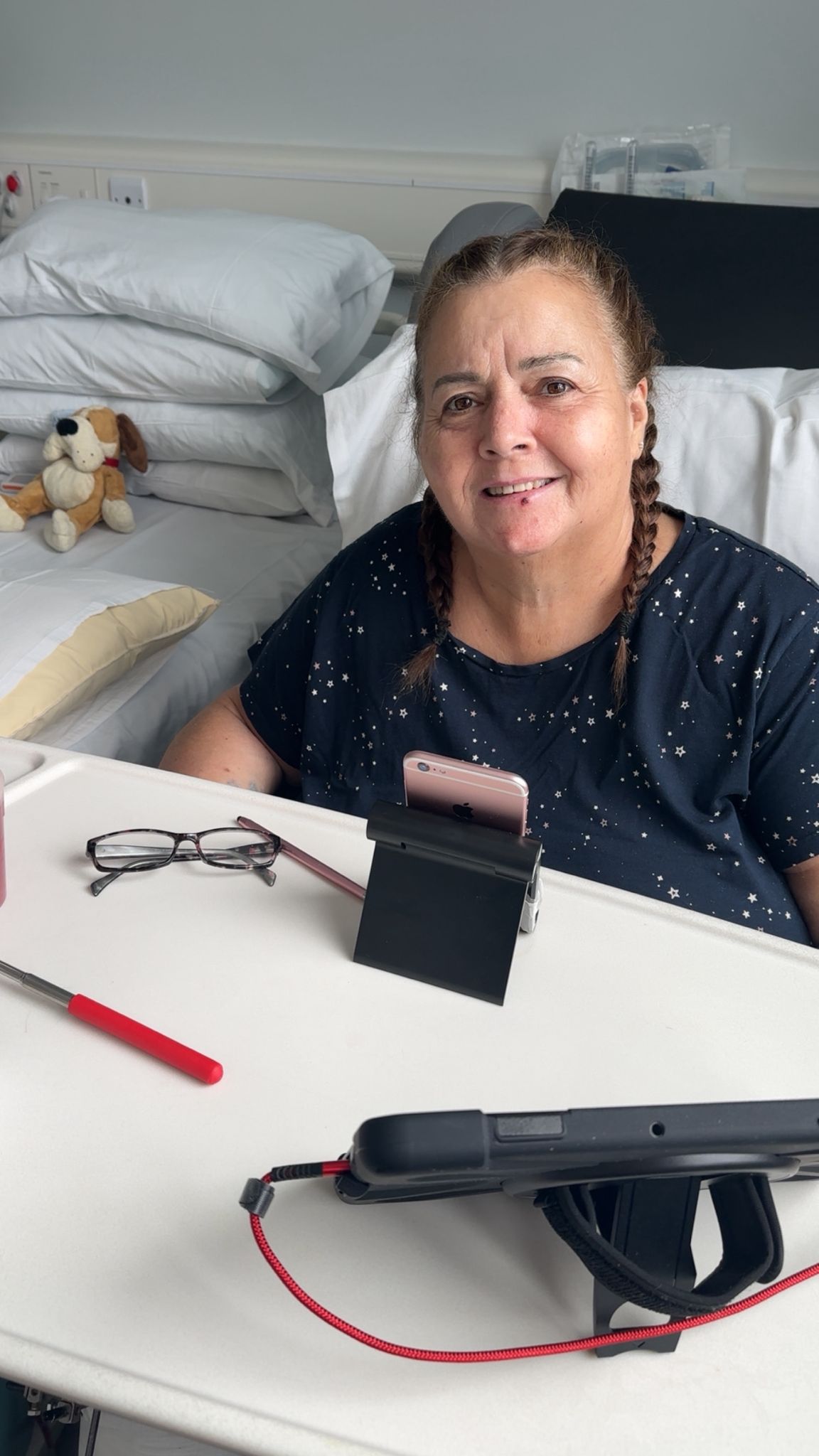 Woman with her hair in plaits and sitting in a hospital bed smiles at the camera